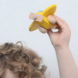 A child holding up a yellow coloured Bajo toy plane with pilot above their head. This plane is part of a wide range of Bajo wooden toy vehicles available at Babipur.