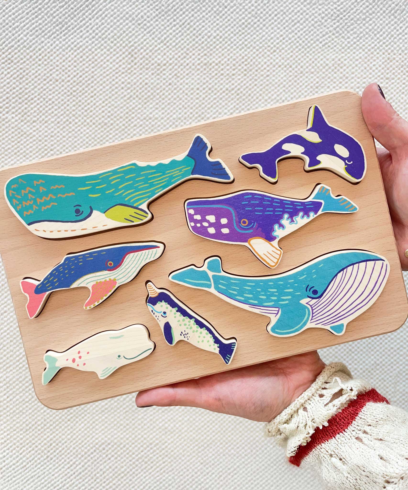 The wooden whale figures shown in the frame held in an adult's hands to show scale. These heirloom quality toys by Bajo are part of a wide range of wooden toys available here at Babipur. 