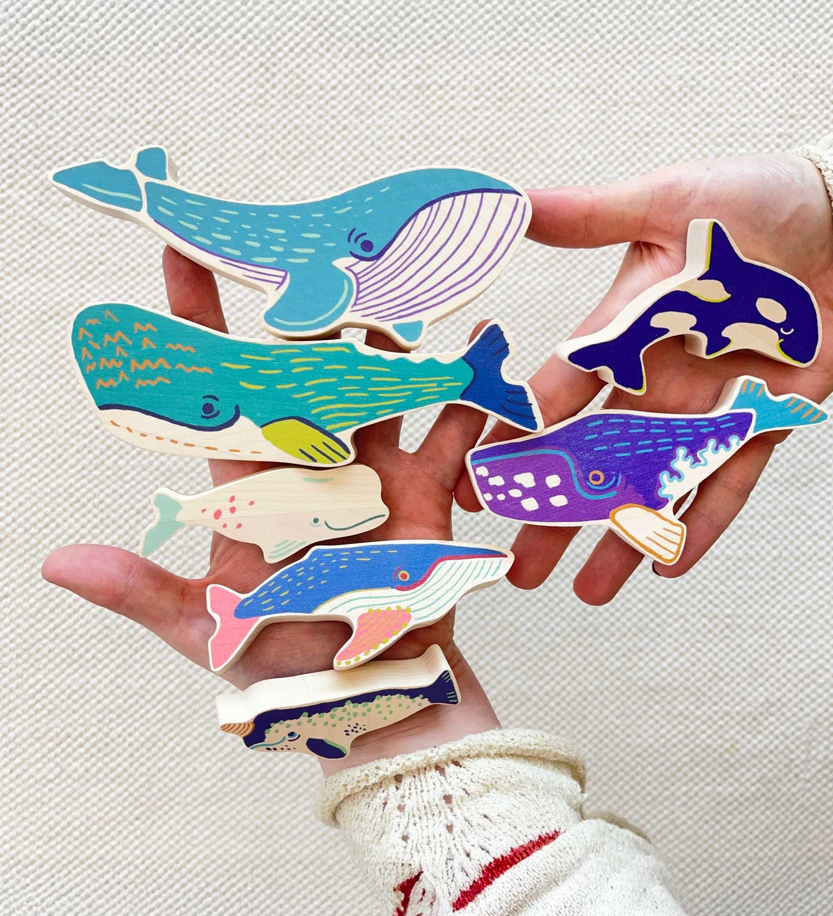 The wooden whale figures shown in an adult's hands to show scale. These heirloom quality toys by Bajo are part of a wide range of wooden toys available here at Babipur. 