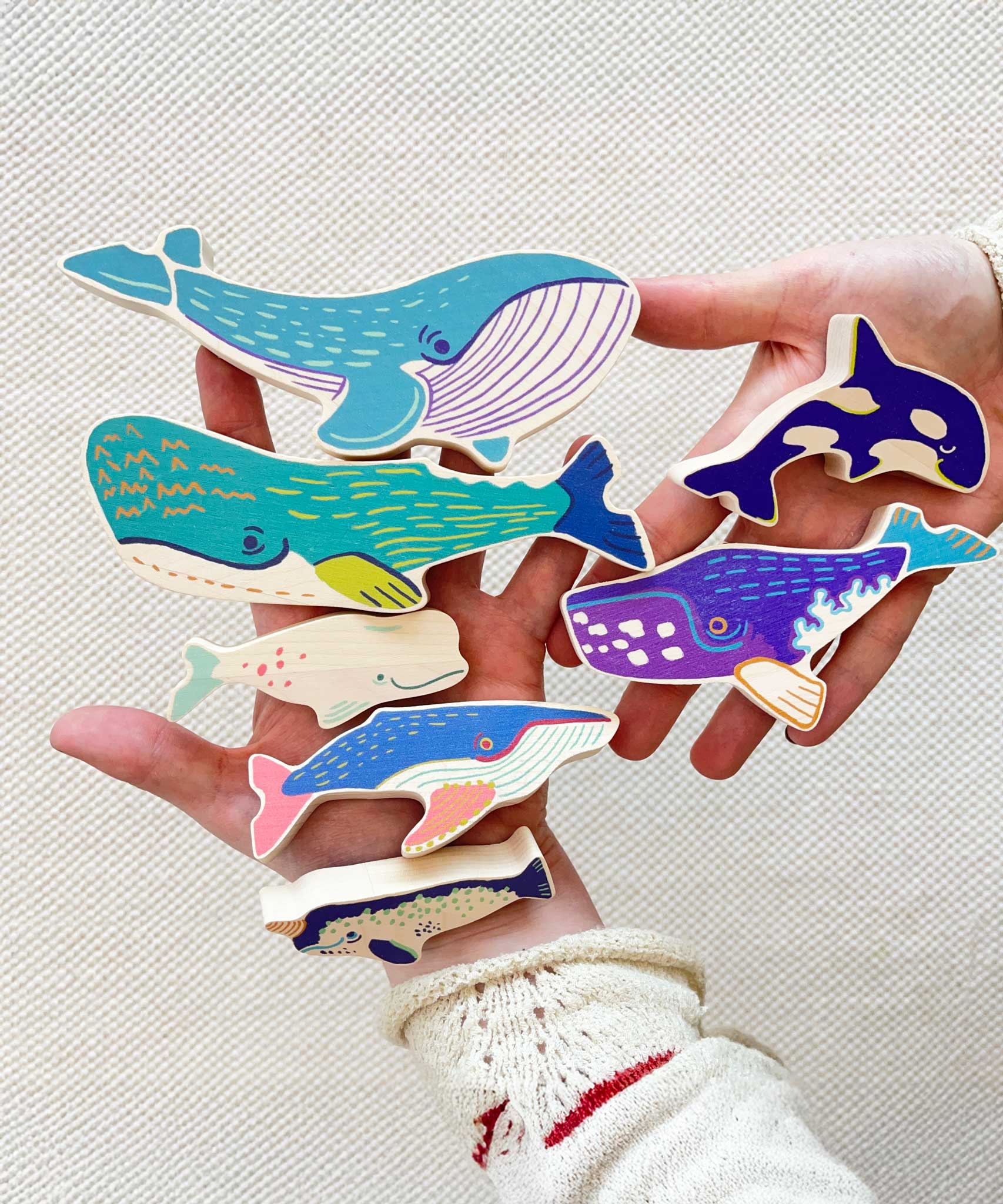 The wooden whale figures shown in an adult's hands to show scale. These heirloom quality toys by Bajo are part of a wide range of wooden toys available here at Babipur. 
