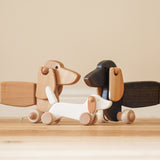 A Bajo white wooden dachshund puppy standing inbetwee the dark oak and natural dachshund pull along dogs available at Babipur