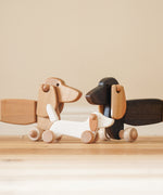 A Bajo white wooden dachshund puppy standing inbetwee the dark oak and natural dachshund pull along dogs available at Babipur