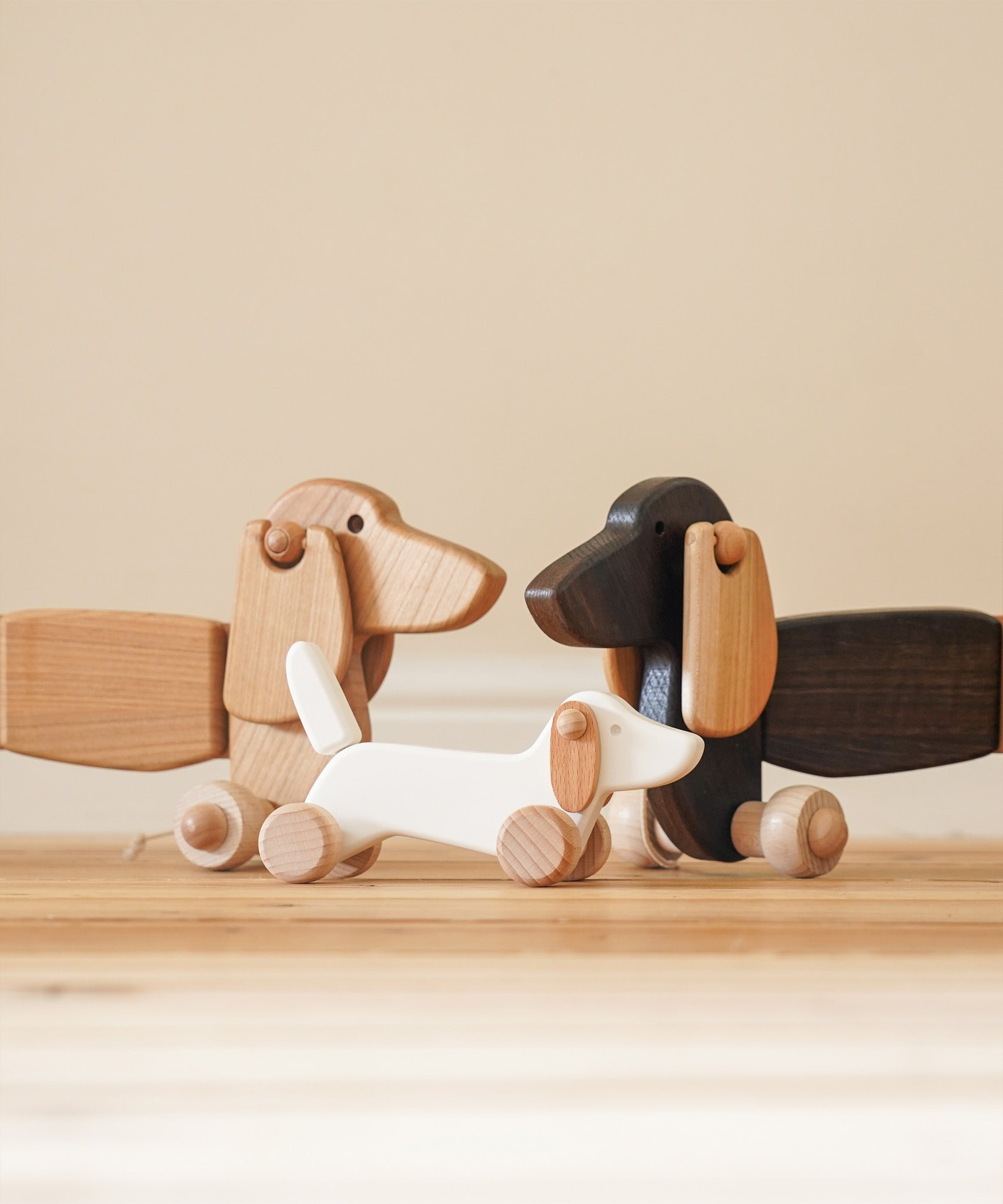 A Bajo white wooden dachshund puppy standing inbetwee the dark oak and natural dachshund pull along dogs available at Babipur