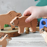A close up of a child's hand placing the wooden bear figure from the  Bajo Wild Animals Forest Set in a small world play scene. A set of 10 wooden forest animal figures that include: Fox, Wolf, Bison, Squirrel, Hedgehog Deer, Hog, Owl, Raccoon and Bear. These heirloom quality toys by Bajo are part of a wide range of wooden toys available here at Babipur.