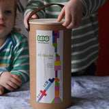Bajo 43 wooden building blocks. 43 blocks, in 16 different shapes and 10 colours. Child lifting the lid off the sturdy cylinder shaped storage box.