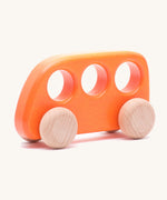 The Bajo push-along bus, a thin wooden bus-shaped toy with three 'window' holes for easy grasping. The main body is painted with non-toxic paints in orange, and the four wheels are left natural to show off the grain.