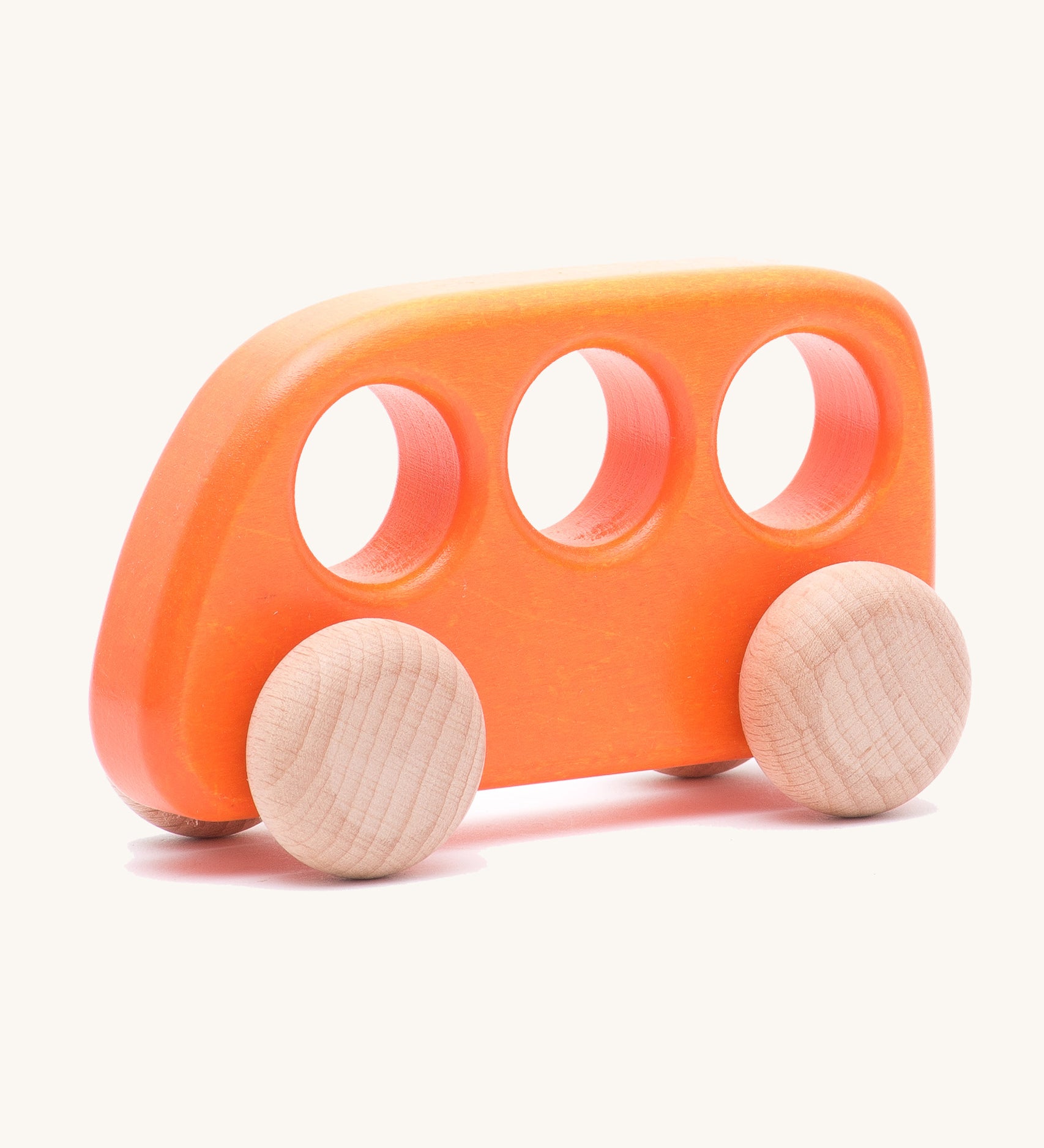 The Bajo push-along bus, a thin wooden bus-shaped toy with three 'window' holes for easy grasping. The main body is painted with non-toxic paints in orange, and the four wheels are left natural to show off the grain.
