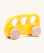 The Bajo push-along bus, a thin wooden bus-shaped toy with three 'window' holes for easy grasping. The main body is painted with non-toxic paints in yellow, and the four wheels are left natural to show off the grain.