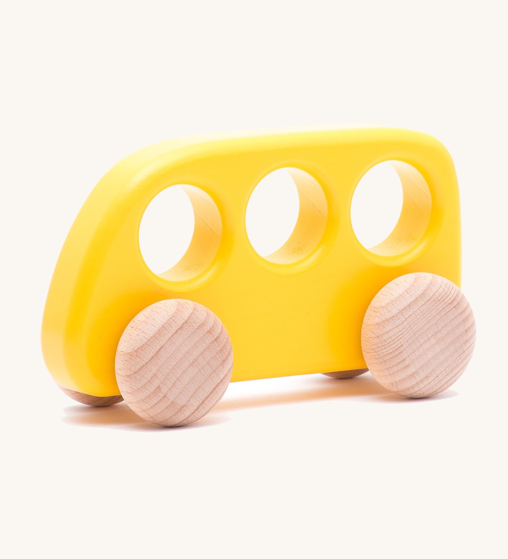 The Bajo push-along bus, a thin wooden bus-shaped toy with three 'window' holes for easy grasping. The main body is painted with non-toxic paints in yellow, and the four wheels are left natural to show off the grain.