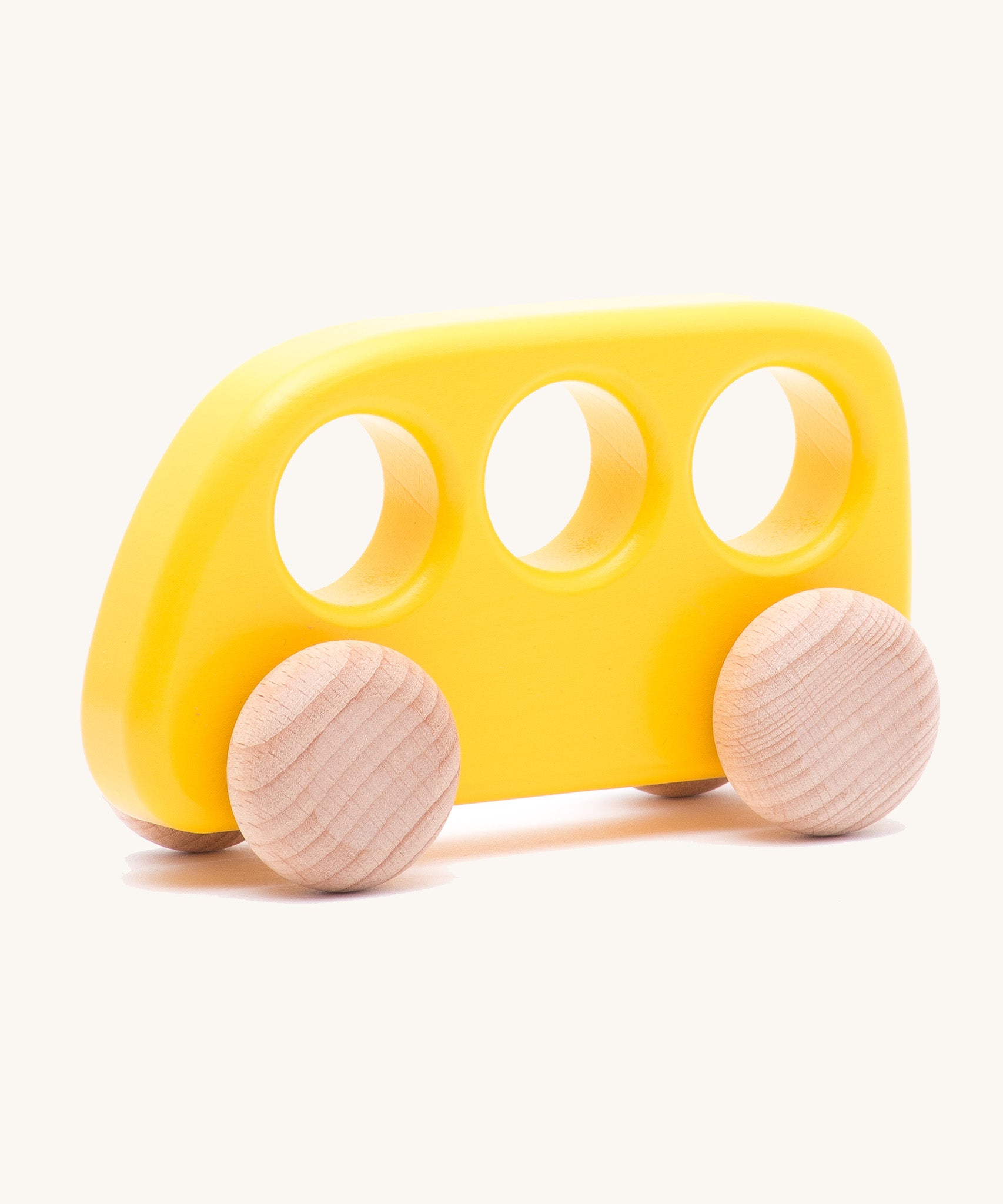 The Bajo push-along bus, a thin wooden bus-shaped toy with three 'window' holes for easy grasping. The main body is painted with non-toxic paints in yellow, and the four wheels are left natural to show off the grain.