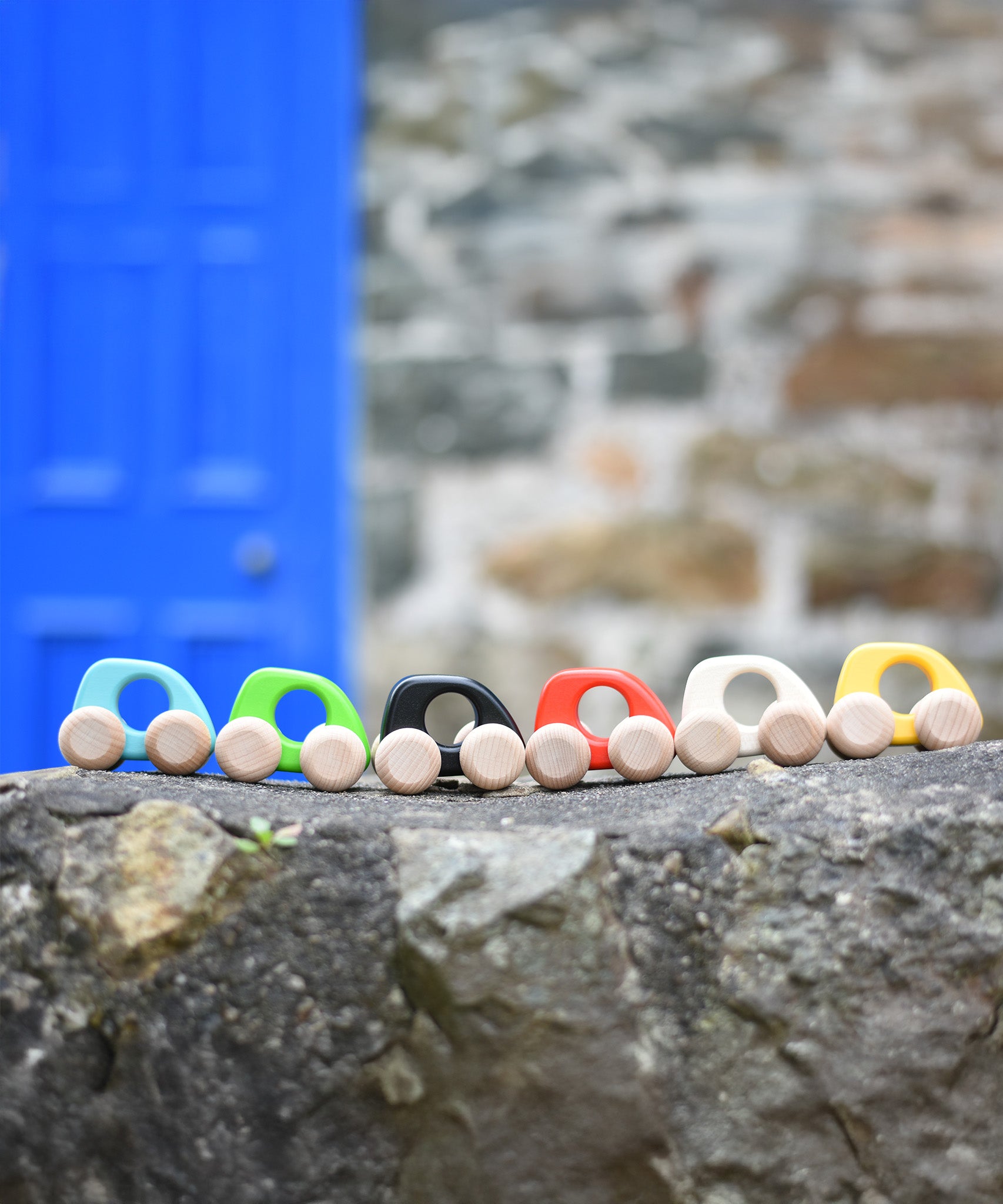 A group of Bajo hand made wooden yellow mini style cars available at Babipur standing on a stone wall