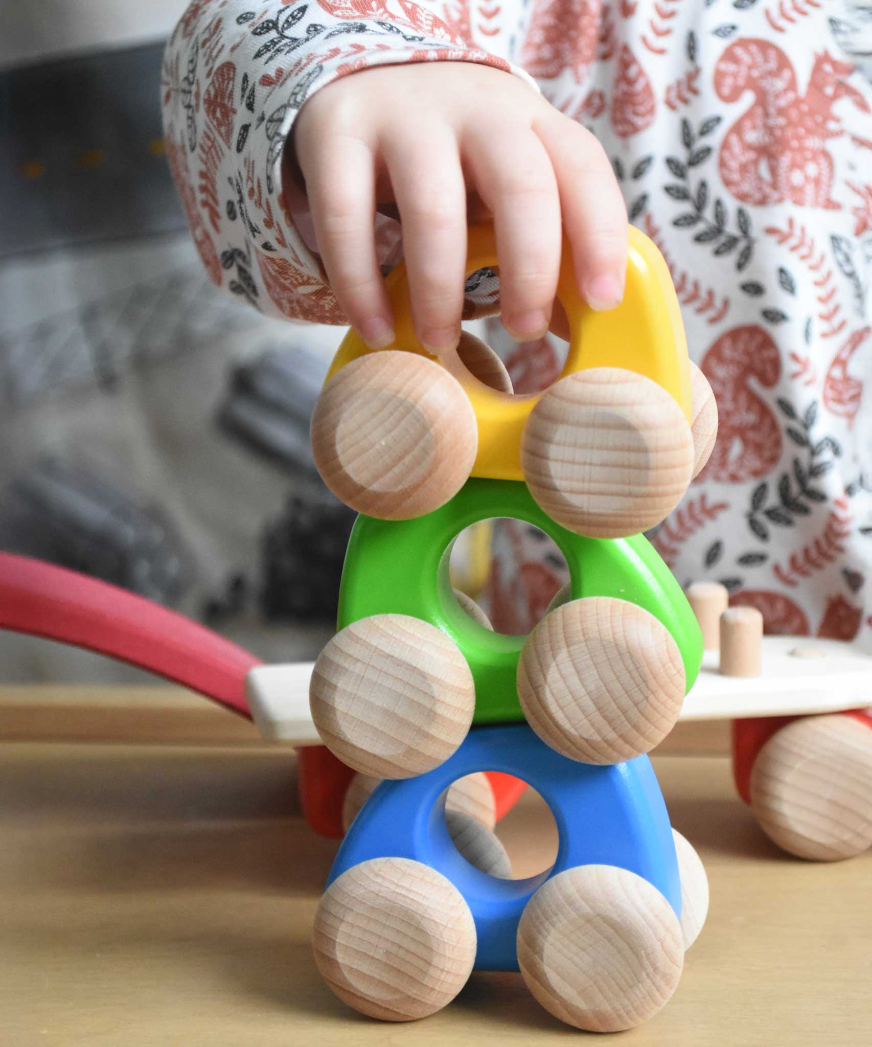A stack of three Bajo mini wooden cars with a child's hand on the car on the top. These heirloom quality toys by Bajo are part of a wide range of wooden toys available here at Babipur. 