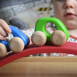 A close up of a child pushing Bajo wooden toy cars along the red piece from the Gluckskafer wooden bridge. These heirloom quality toys by Bajo are part of a wide range of wooden toys available here at Babipur. 