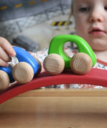 A close up of a child pushing Bajo wooden toy cars along the red piece from the Gluckskafer wooden bridge. These heirloom quality toys by Bajo are part of a wide range of wooden toys available here at Babipur. 