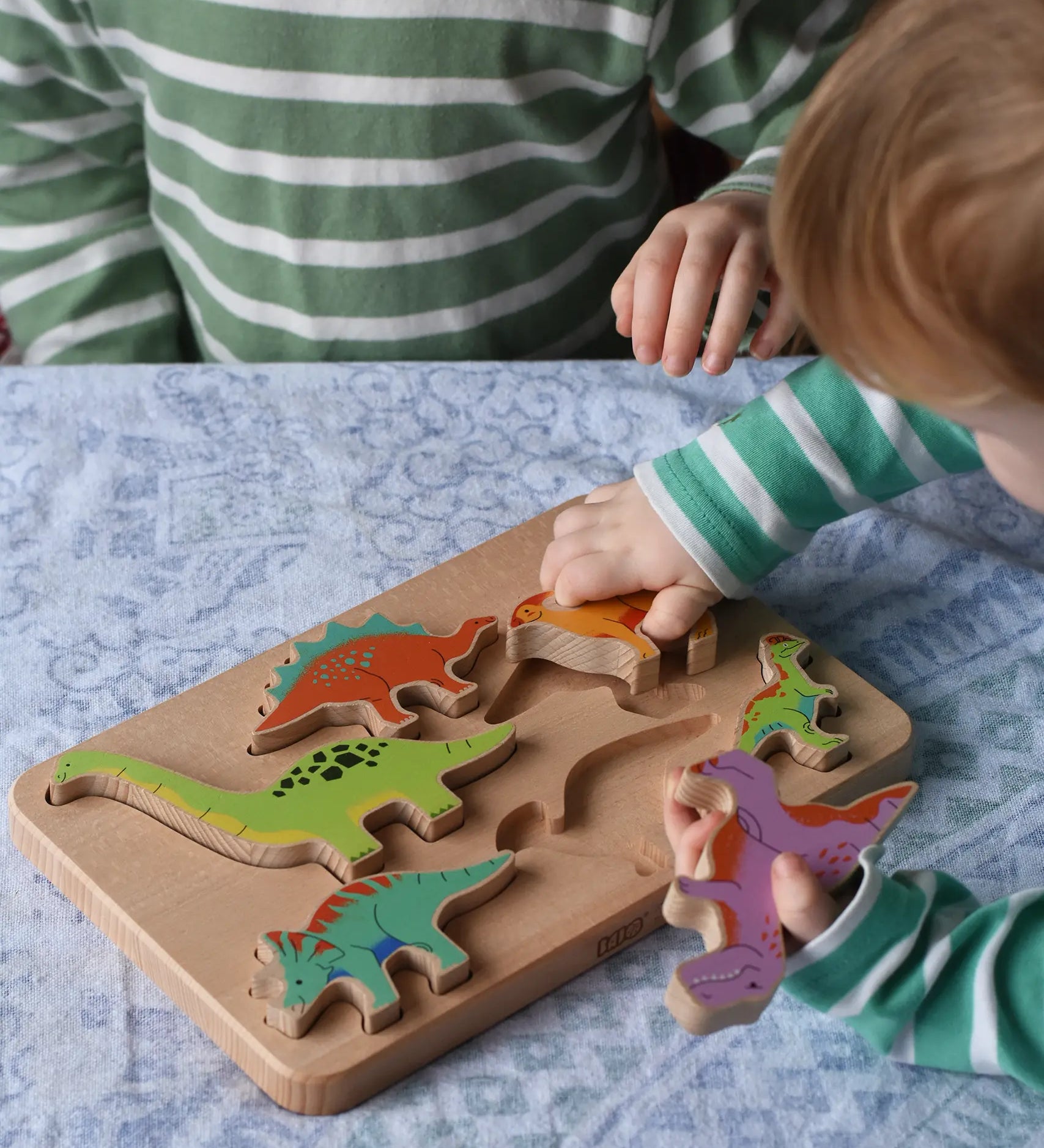 Bajo Wooden Dinosaur Puzzle with 6 colourful figures. Children placing the figures into the shaped slots on the base.