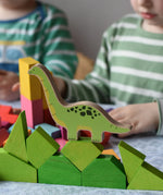Brontosaurus Bajo Wooden Dinosaur Puzzle figure piece placed on green building blocks. Children playing in background.