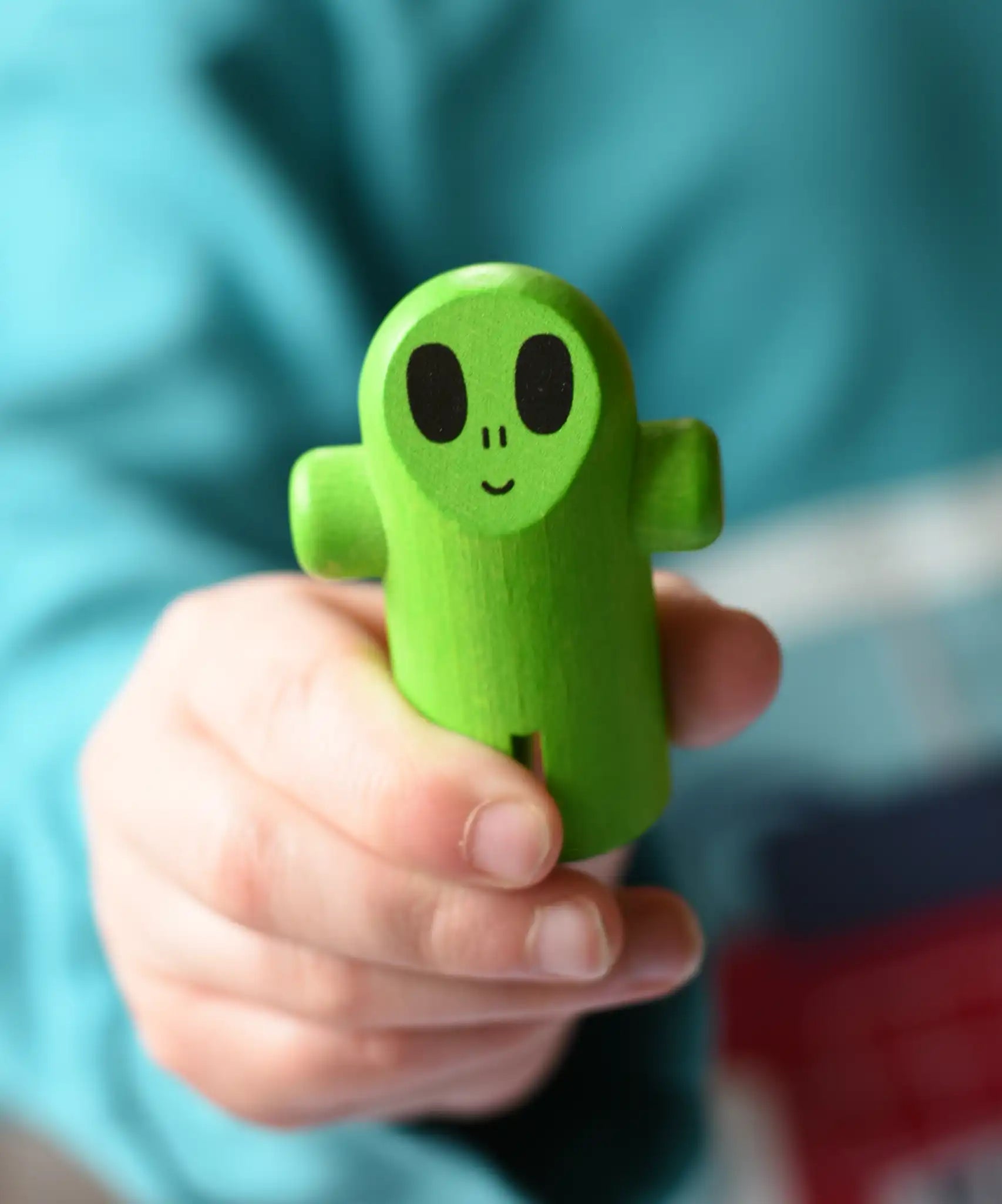 Close up of the green alien figure from the Bajo Flying Saucer set in a child's hand.