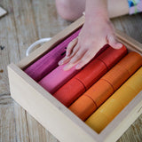 Child's hand resting on the coloured cylinders from the Bajo fraction set inside a wooden storage box