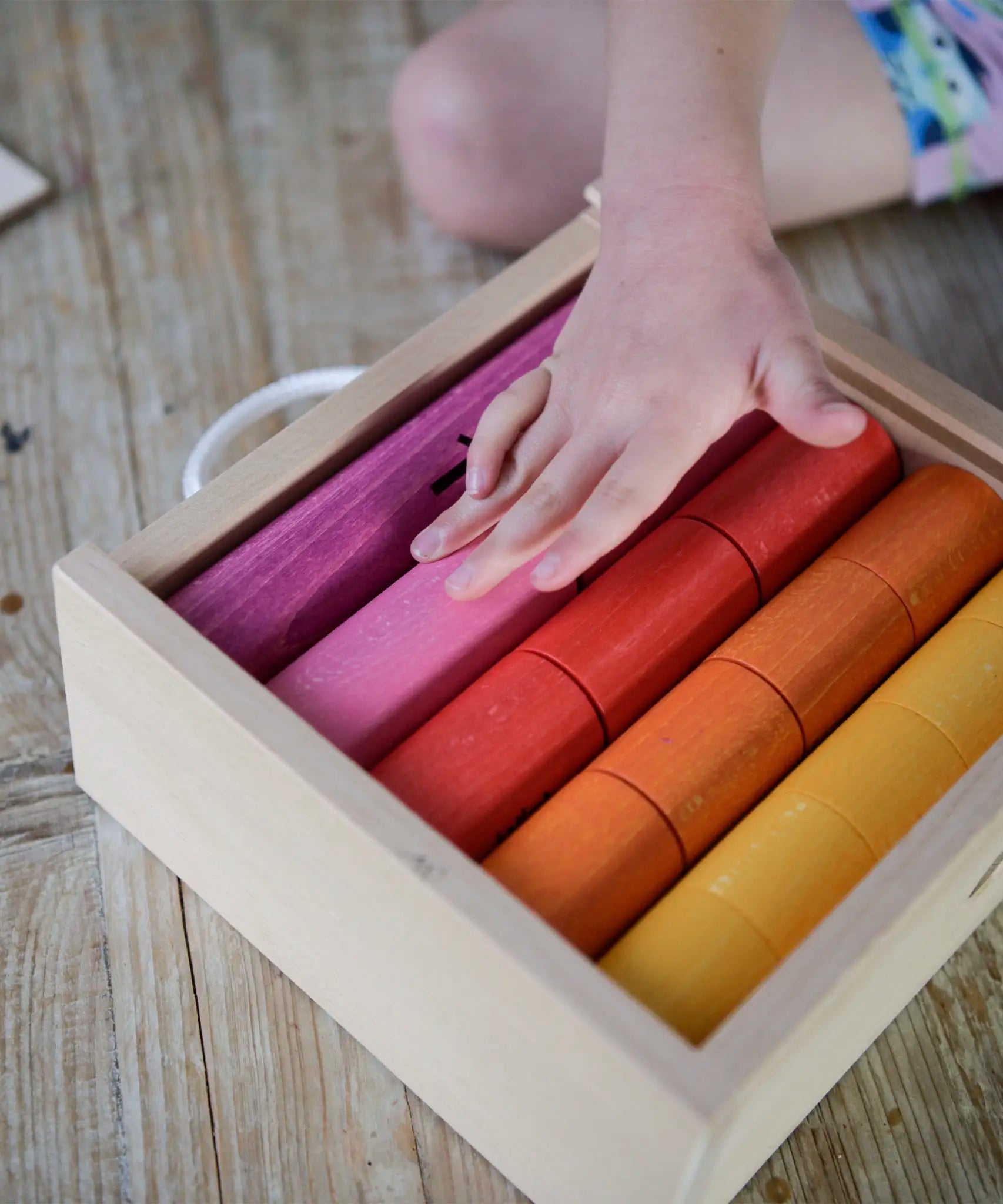 Child's hand resting on the coloured cylinders from the Bajo fraction set inside a wooden storage box