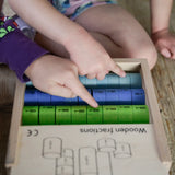 Children pointing at different coloured wooden disks from the Bajo fraction set showing their fractions painted in black