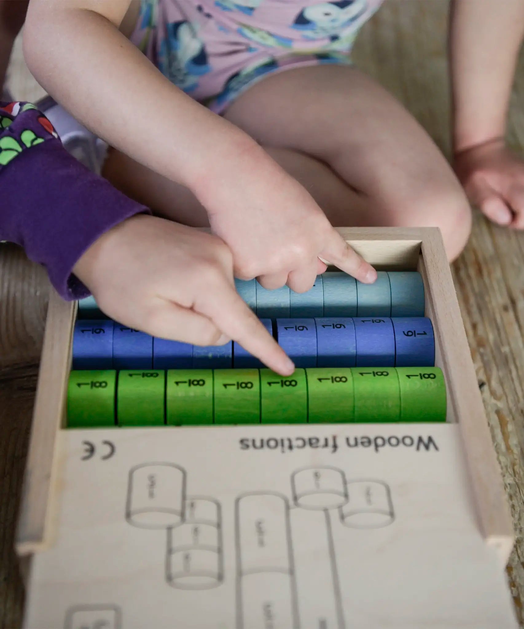 Children pointing at different coloured wooden disks from the Bajo fraction set showing their fractions painted in black