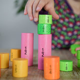 A close up of a child's hand playing with the Bajo Fractions Set. A set of coloured wooden blocks marked with fractions on each block. These heirloom quality toys by Bajo are part of a wide range of wooden toys available here at Babipur.