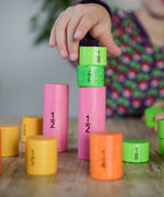 A close up of a child's hand playing with the Bajo Fractions Set. A set of coloured wooden blocks marked with fractions on each block. These heirloom quality toys by Bajo are part of a wide range of wooden toys available here at Babipur.
