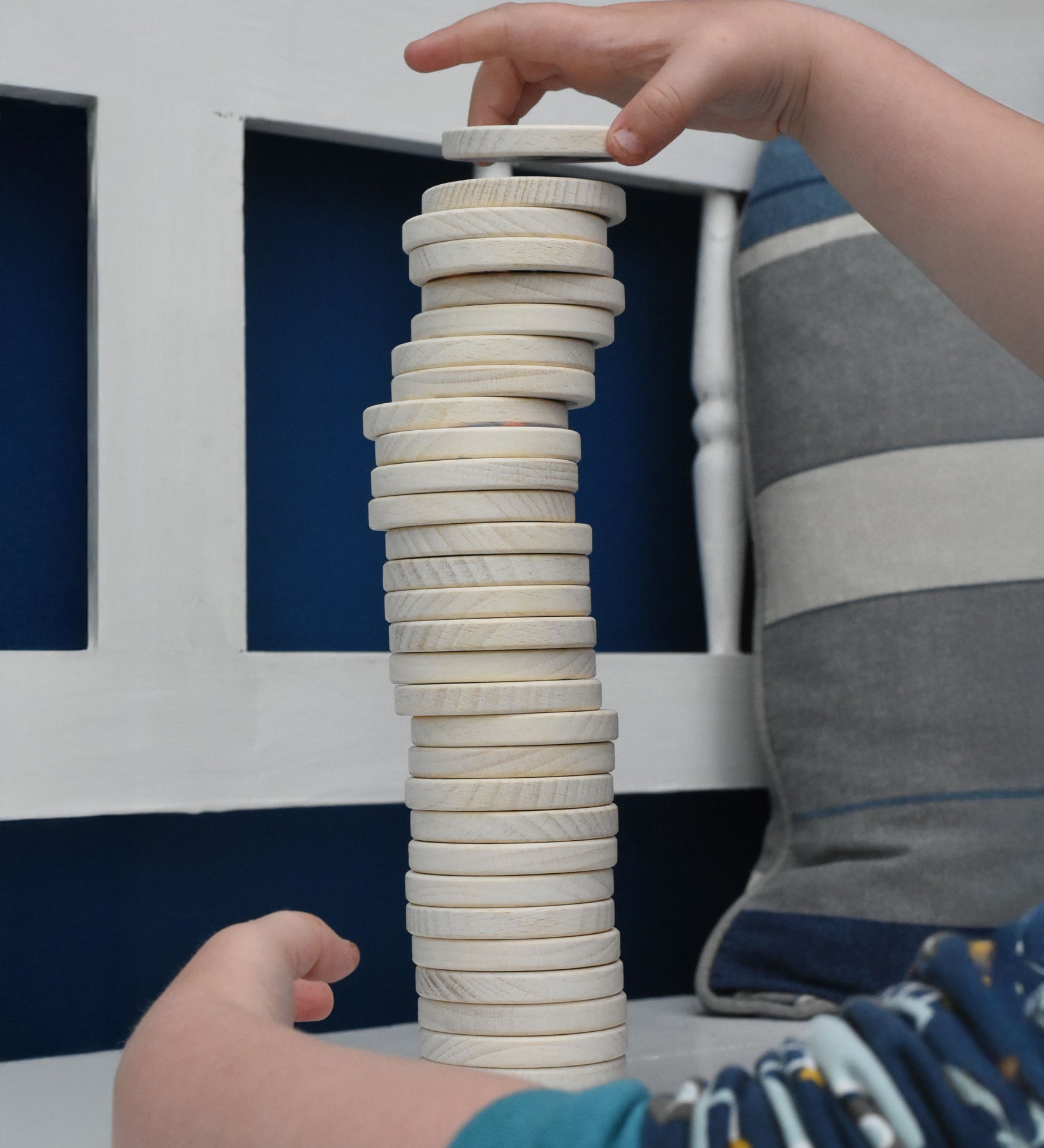 A close up of a child's hand stacking the wooden dics from a Bajo Memory Game on top of each other. These heirloom quality toys by Bajo are part of a wide range of wooden toys available here at Babipur.