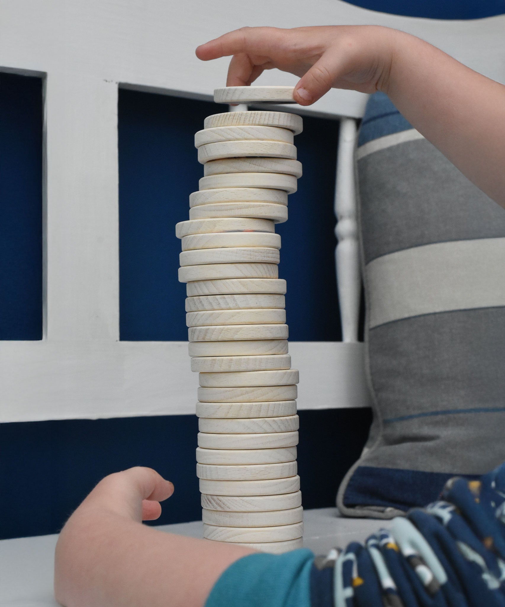 A close up of a child's hand stacking the wooden dics from a Bajo Memory Game on top of each other. These heirloom quality toys by Bajo are part of a wide range of wooden toys available here at Babipur.