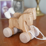 Bajo hand made wooden natural jumping horse available at Babipur. Features unpainted wheels and a toggle to pull along. Horses are standing on a wooden surface 
