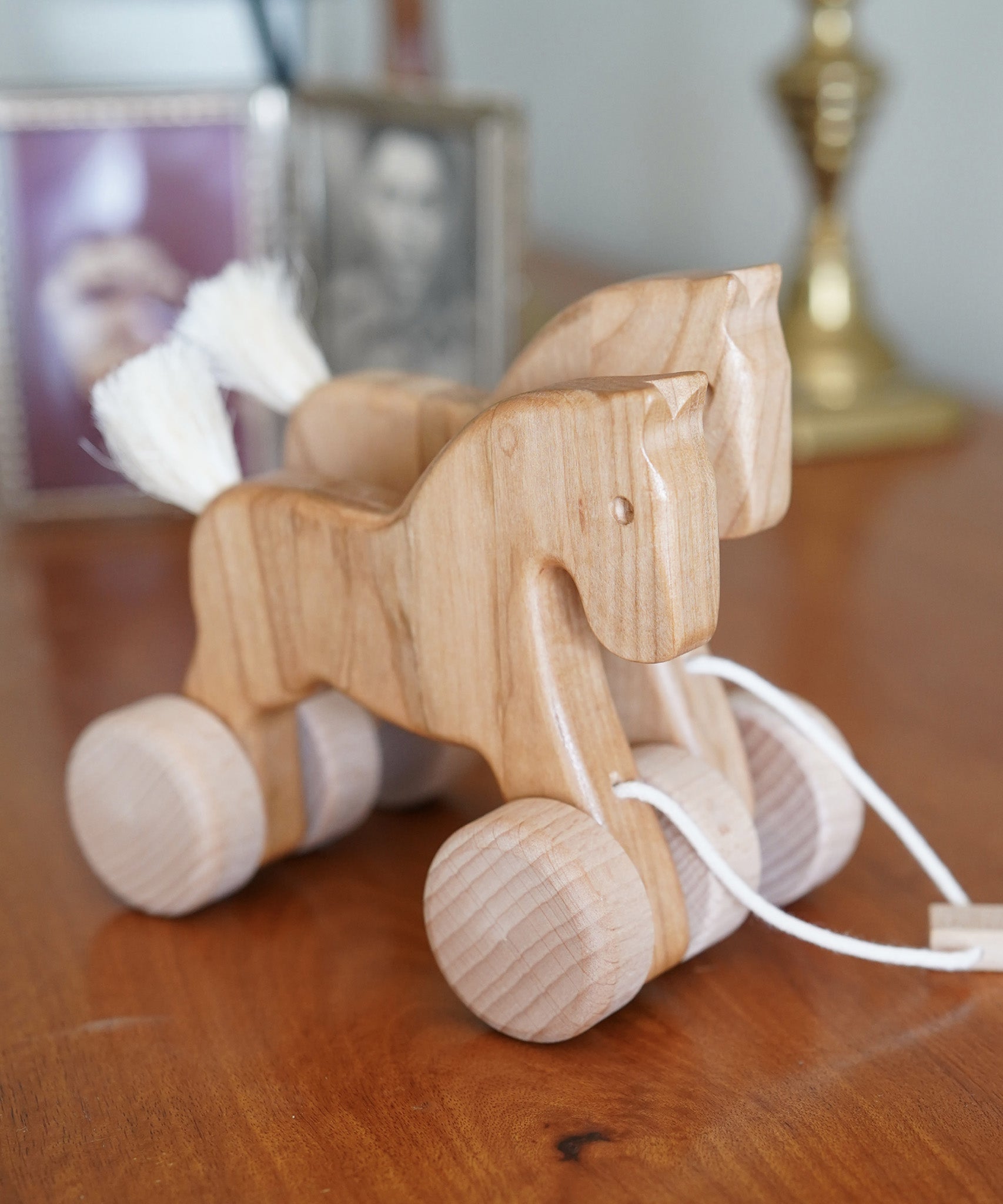 Bajo hand made wooden natural jumping horse available at Babipur. Features unpainted wheels and a toggle to pull along. Horses are standing on a wooden surface 