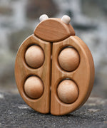 Bajo natural wooden ladybird teether placed on a stone wall outdoors in the Babipur garden.
