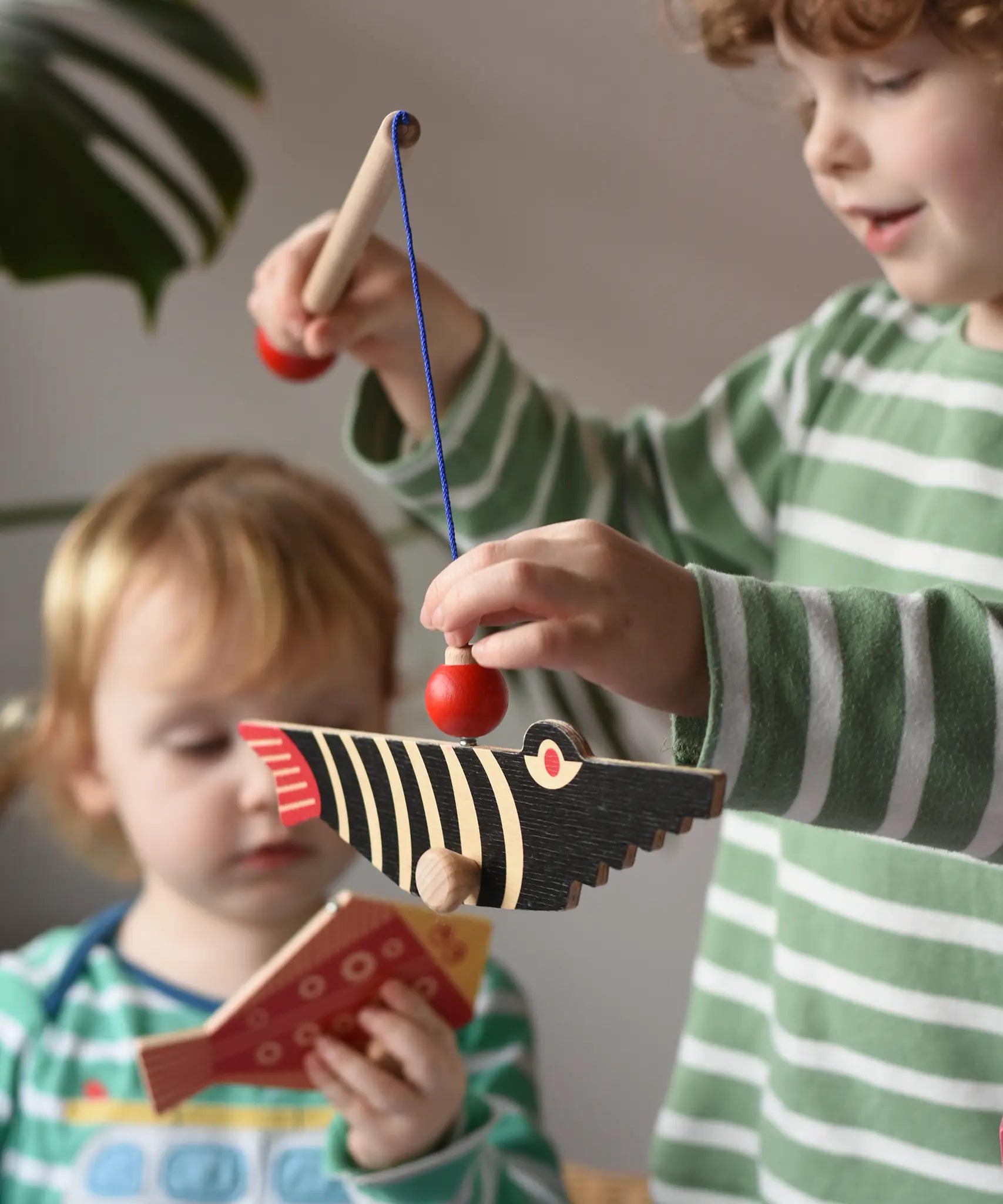 Bajo magnetic fishing game toy. Child holding wooden rod with black fish attached.