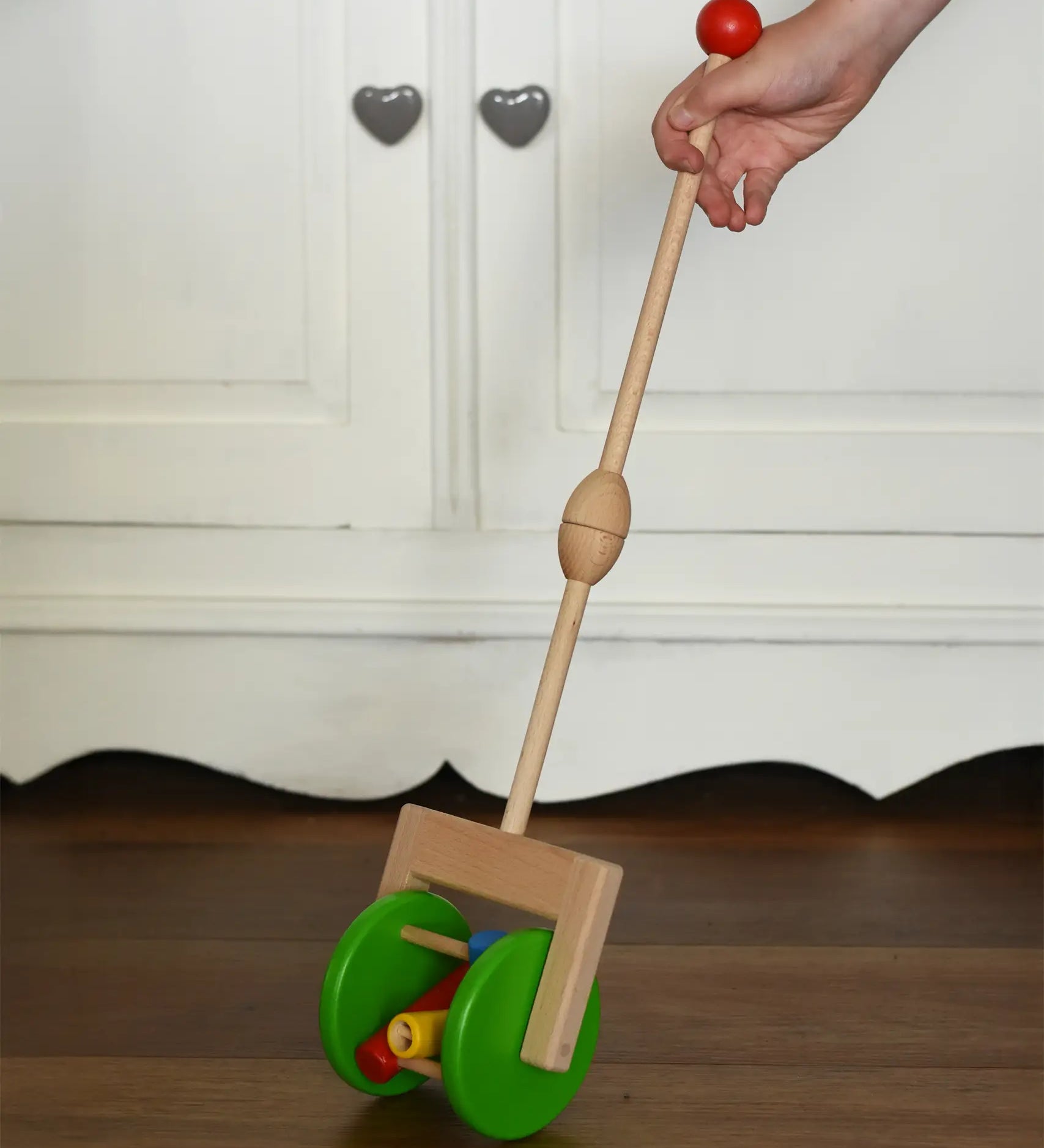 Bajo push along wooden toy rattle in a child's hand. Green rollers with coloured pieces in the middle attacked to a stick.