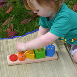 Bajo sorting board wooden toy played with by a child who is stacking Nin peg dolls on top of the coloured shapes.