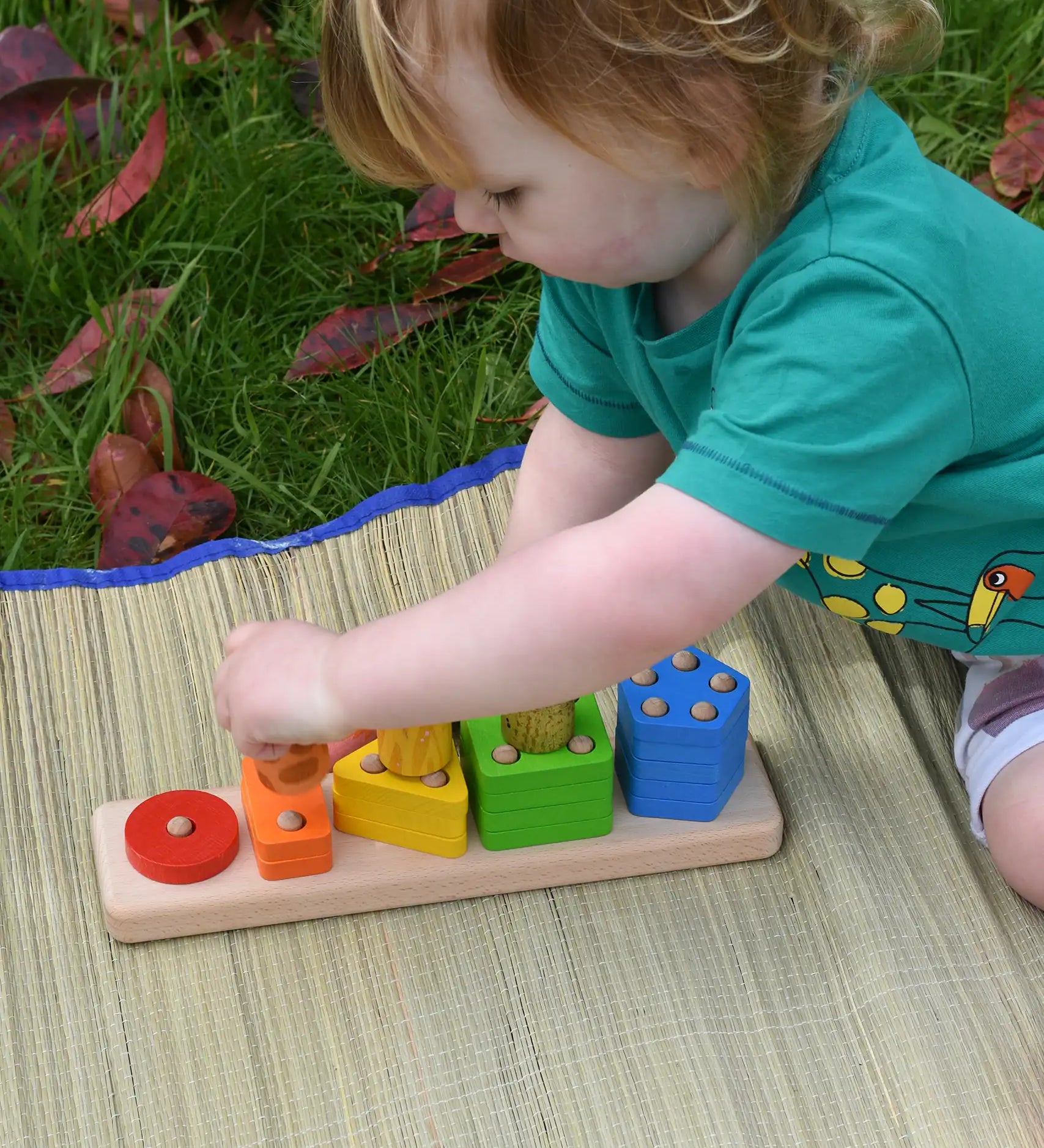 Bajo sorting board wooden toy played with by a child who is stacking Nin peg dolls on top of the coloured shapes.