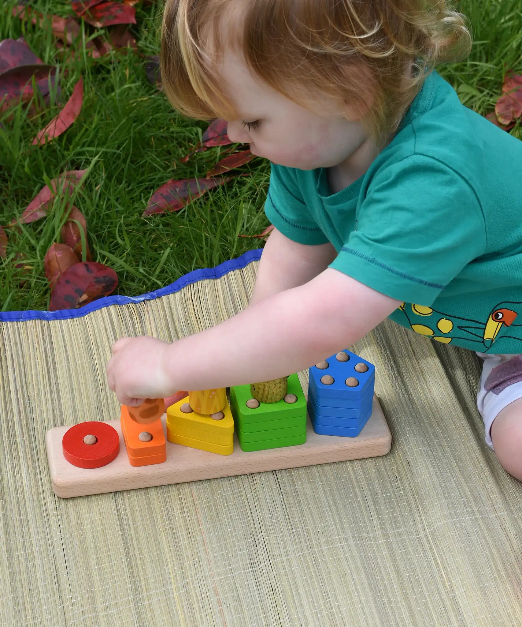 Bajo sorting board wooden toy played with by a child who is stacking Nin peg dolls on top of the coloured shapes.