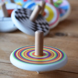 Bajo Colourful Circles Spinning Top spinning an d blurred in motion on a wooden surface. Other spinning top toys can be seen in the background. 