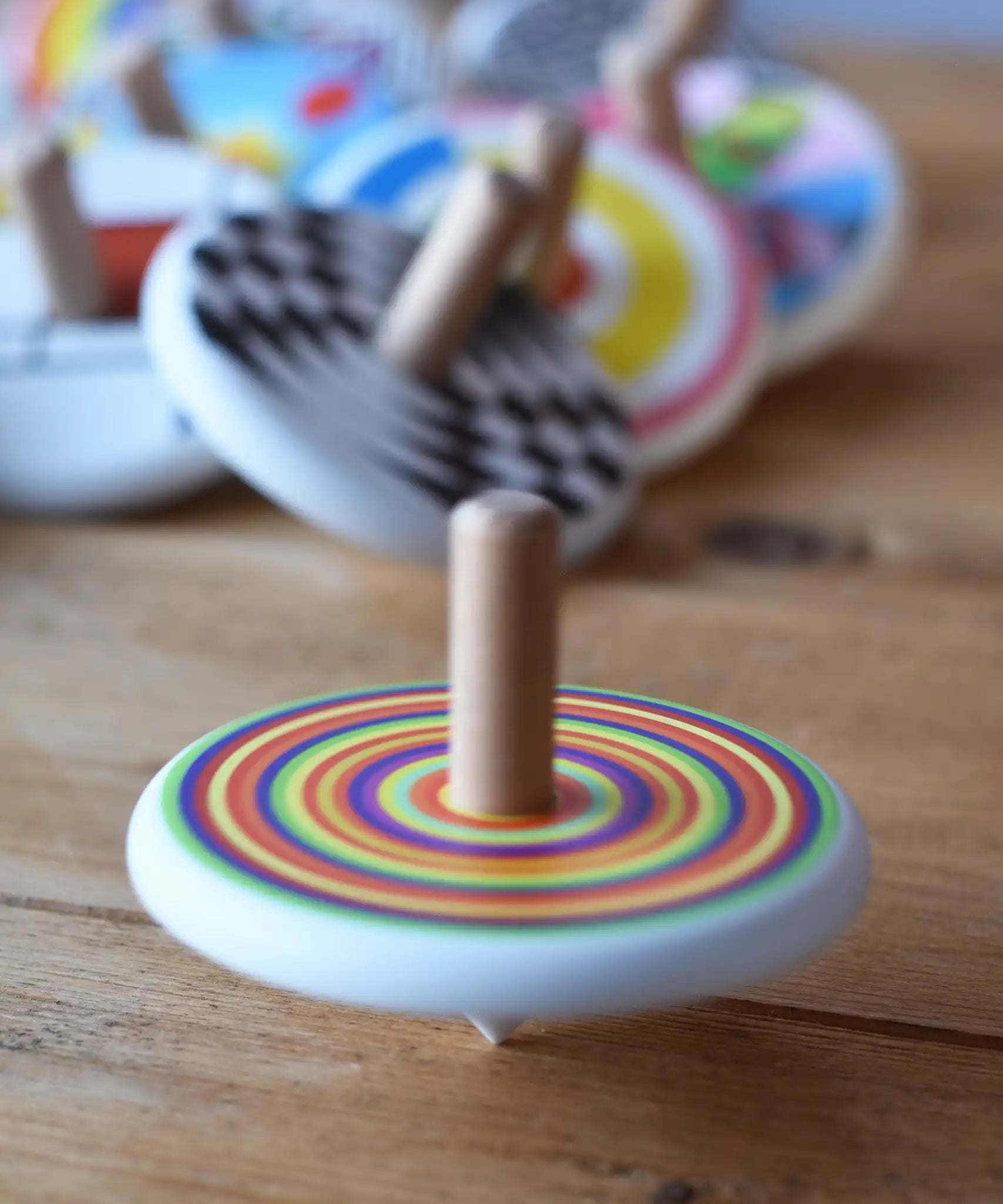 Bajo Colourful Circles Spinning Top spinning an d blurred in motion on a wooden surface. Other spinning top toys can be seen in the background. 