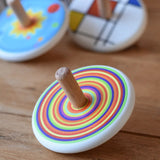 Bajo Colourful Circles Spinning Top placed on a wooden surface with other wooden spinning tops in the background.