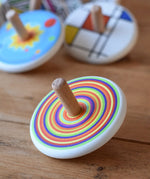 Bajo Colourful Circles Spinning Top placed on a wooden surface with other wooden spinning tops in the background.