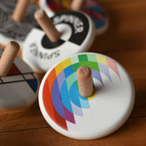 Bajo Echo Spinning Top placed on a wooden surface with other wooden spinning tops in the background. 