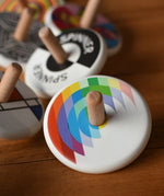 Bajo Echo Spinning Top placed on a wooden surface with other wooden spinning tops in the background. 