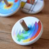 Bajo Echo Spinning Top placed on a wooden surface with other wooden spinning tops in the background. 