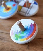 Bajo Echo Spinning Top placed on a wooden surface with other wooden spinning tops in the background. 
