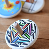 Bajo Modern Colour Spinning Top placed on a wooden surface with other wooden spinning tops in the background. 
