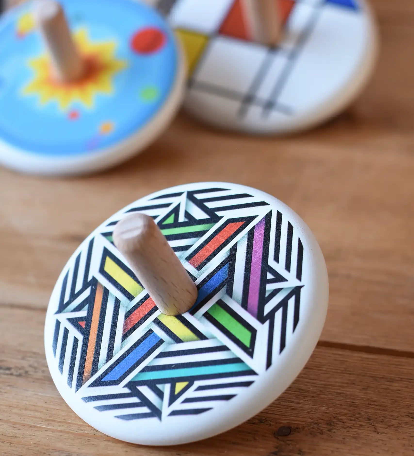 Bajo Modern Colour Spinning Top placed on a wooden surface with other wooden spinning tops in the background. 