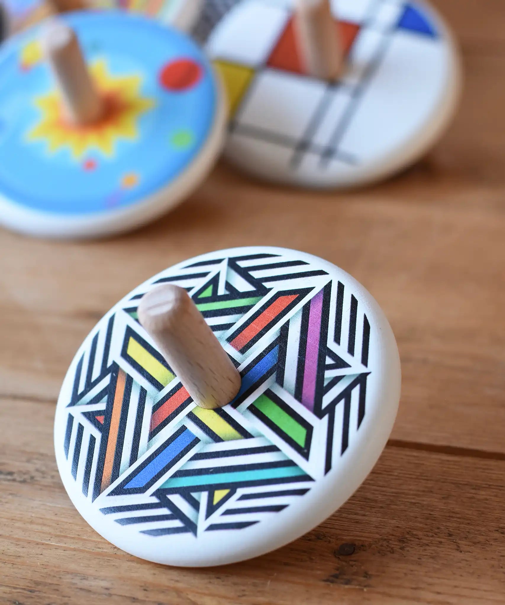 Bajo Modern Colour Spinning Top placed on a wooden surface with other wooden spinning tops in the background. 