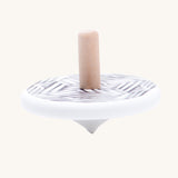 The Bajo Modern wooden Spinning Top toy shown blurred in motion as it spins around. A white painted spinning top with a natural wooden stick. The top features a black and white mono striped design.