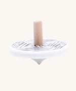 The Bajo Modern wooden Spinning Top toy shown blurred in motion as it spins around. A white painted spinning top with a natural wooden stick. The top features a black and white mono striped design.
